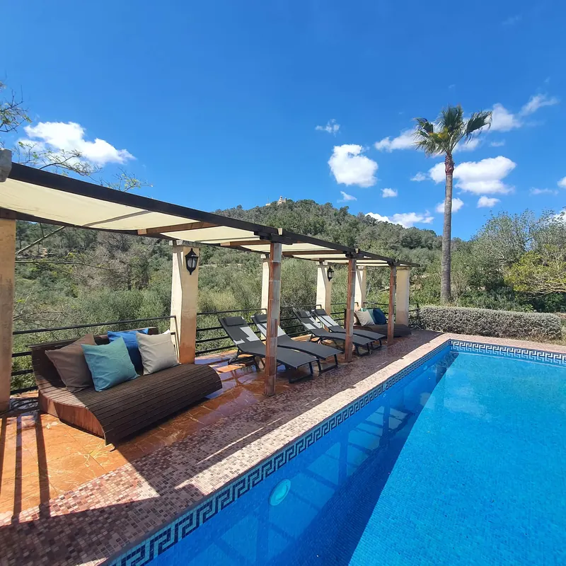 Piscina con tumbonas bajo una pérgola y el monte de Bonany al fondo